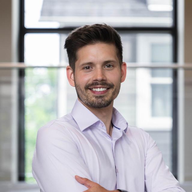 Damian Dudka standing in front of a window smiling
